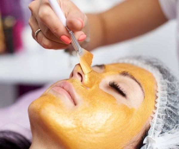 Macro photography of the hand of the beautician with the help of a special brush puts on the face of the girl a golden mask in the spa